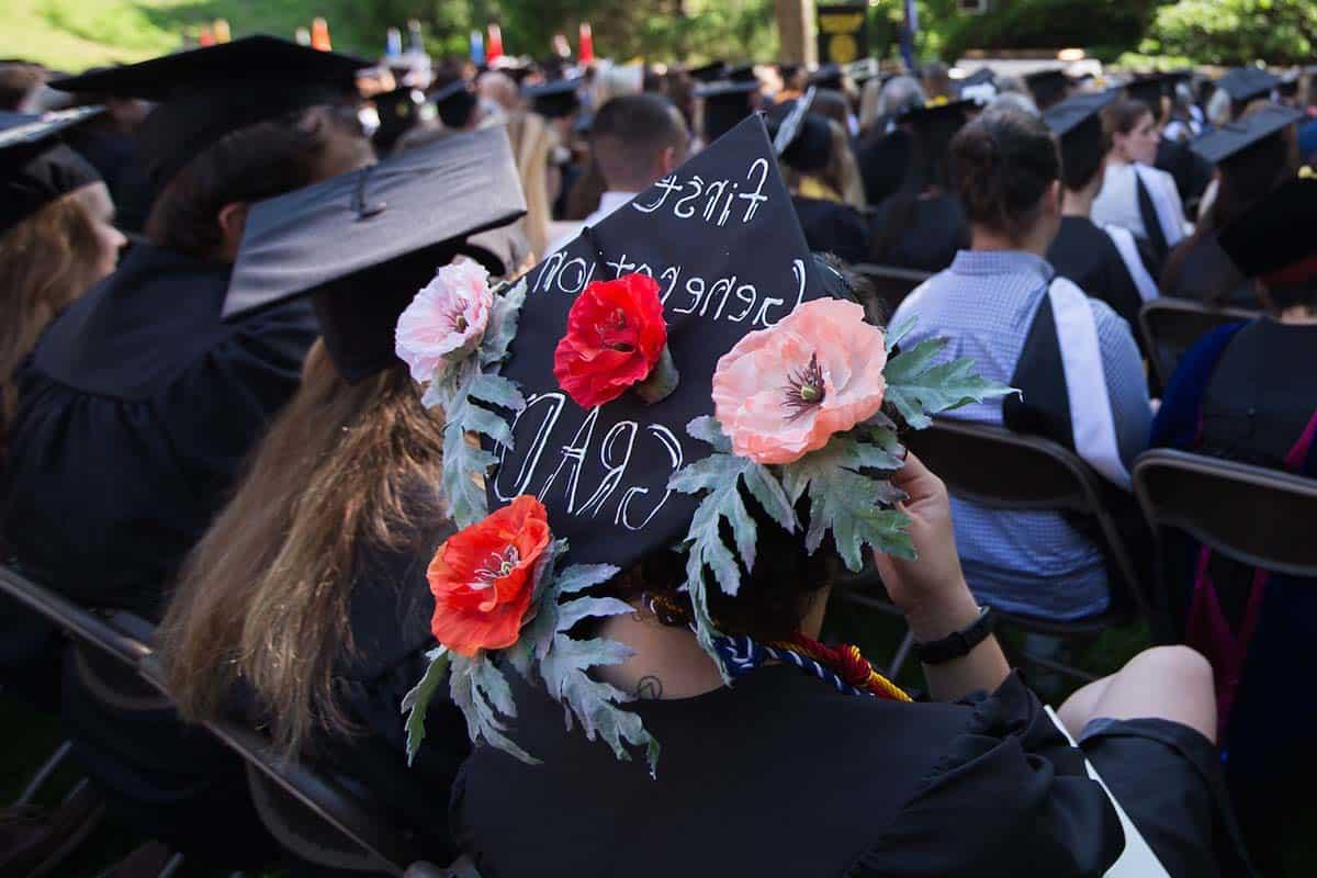 Graduating student wears a cap decorated with flowers and the words First Generation Grad.