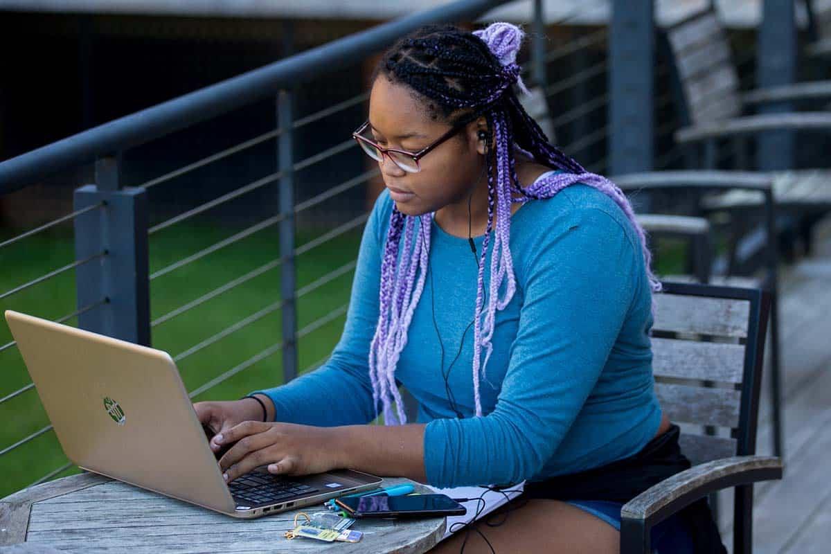 Female student works on her wi-fi connected laptop on the patio outside the Student Center.